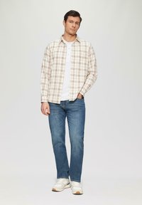 Geruite langemouwhemd in beige en bruin, gedragen over een witte crew-neck t-shirt, gecombineerd met blauwe jeans en witte sneakers.