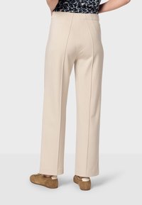 Beige wijde broek met een soepele textuur, voorzien van een hoge taille en voorplooien. In combinatie met bruine suède schoenen.