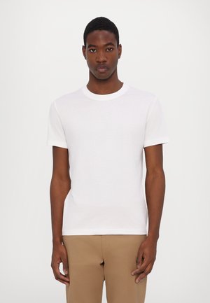 Camiseta blanca de manga corta con escote redondo, hecha de un material de algodón suave, combinada con pantalones beiges.
