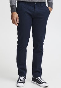 Chinos azul marino de mezcla de algodón, con dos bolsillos laterales y cierre de botón, combinados con zapatillas negras y blancas.