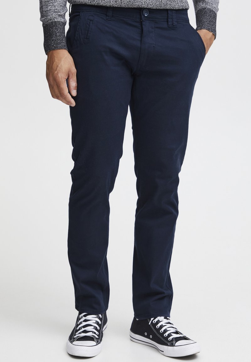 Chinos azul marino de mezcla de algodón, con dos bolsillos laterales y cierre de botón, combinados con zapatillas negras y blancas.