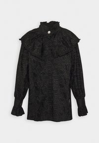 Blouse noire avec col montant à volants, broderies florales et détails découpés. Manches longues avec poignets à volants. Tissu texturé.