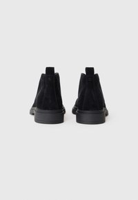 Botas de tobillo de ante negro con suela de goma, que cuentan con una asa en la parte posterior y una textura suave, diseñadas para la comodidad y el estilo.