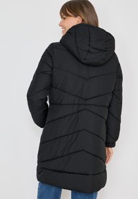 Sort pufferjakke med hætte, chevron-syninger og elastiske manchetter. Stoffet har en subtil tekstur og en mid-længde skæring.