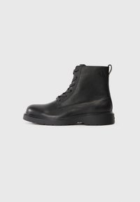 Botín negro de tobillo hecho de cuero texturizado con punta redonda, diseño con cordones y una resistente suela de goma negra. Presenta un lazo en el talón.