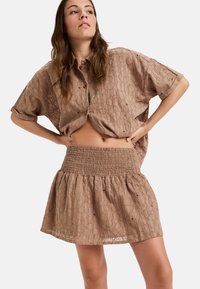 Bruine getextureerde twee-delige outfit bestaande uit een korte mouwen overhemd met knopen en een rok met smock taille, een uitlopende zoom en patroondetails.
