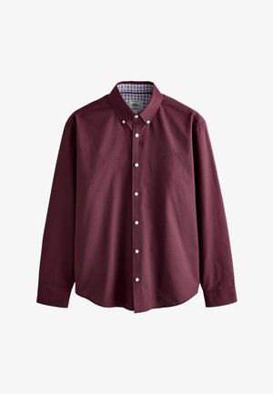 Chemise à manches longues couleur bordeaux avec col boutonné et boutons blancs, dotée d'une doublure intérieure à carreaux sur le col.