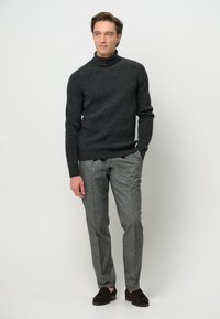 Dunkelgrauer gerippter Rollkragenpullover, kombiniert mit hellgrauen maßgeschneiderten Hosen und dunkelbraunen Slippern. Sauberes Design mit taillierter Silhouette.