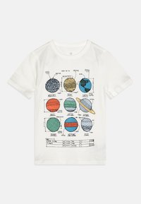 T-shirt en coton blanc avec un imprimé coloré de planètes disposées en grille, avec les noms et les mesures en dessous de chaque illustration.