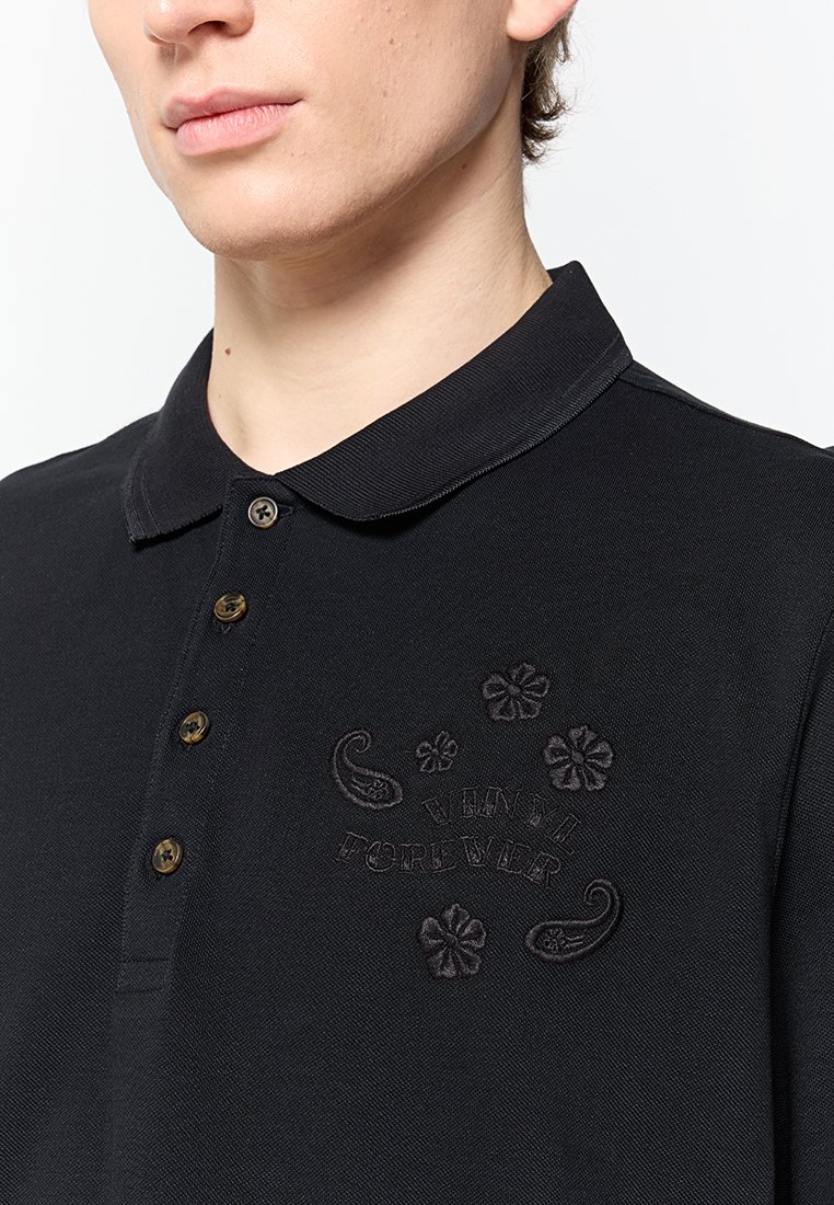 Polo noir en tissu texturé, doté d'un col, de trois boutons et d'accents brodés avec des motifs floraux sur la poitrine.