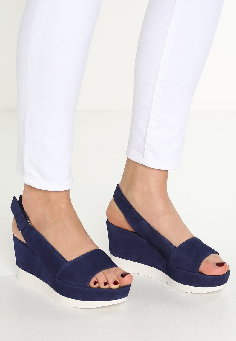 Sandales compensées en daim bleu marine avec bouts ouverts et design à bride arrière, dotées d'une semelle blanche texturée et d'accents minimalistes.