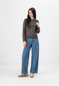 Polo brun à manches longues avec patte de boutonnage, associé à un jean bleu à jambe large. Les chaussures présentent un imprimé léopard. Sac à main noir, au design minimaliste.