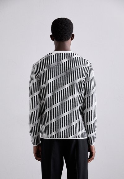 Μαύρο και λευκό πουλόβερ πλεκτό με κάθετες ρίγες, υφή και στρογγυλή λαιμόκοψη. Οι μακριές μανίκες είναι εφαρμοστοί στους καρπούς.