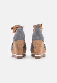 Talons compensés en daim gris avec des détails en liège, des brides de cheville beiges et une semelle blanche. Présente une forme arrondie et des côtés ouverts pour la ventilation.