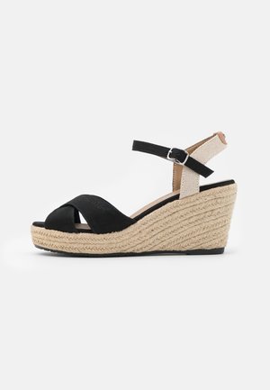 Black wedge sandals with woven jute heel, featuring a crossed upper design and an adjustable ankle strap made from a textured fabric.