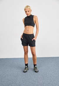 Zwarte geribbelde crop top en bijpassende shorts, beide met een aansluitend ontwerp. Model draagt zwarte sneakers met gele accenten tegen een effen achtergrond.