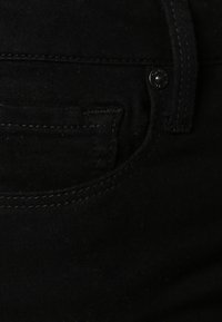 Tissu en denim noir avec un gros plan sur une petite poche, présentant des coutures ton sur ton et un détail de bouton en métal sur la ceinture.