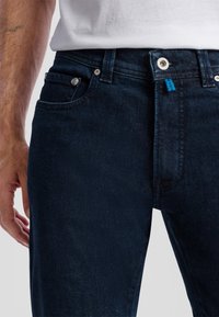 Donkerblauwe denim spijkerbroek met een slim fit, met vijf zakken, zilveren hardware en een blauwe labelaccent op de tailleband.
