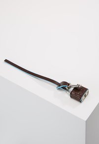 Portachiavi con lucchetto in pelle marrone con accenti blu, caratterizzato da un design compatto e hardware in argento. Chiave attaccata alla cinghia.