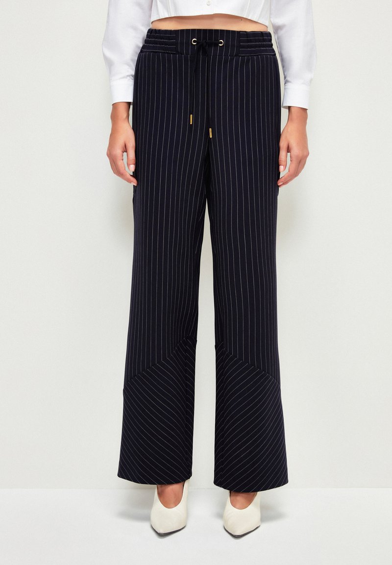 Marineblaue weit geschnittene Hose mit vertikalen Streifen, ausgestattet mit einem Kordelzugbund, Fronttaschen und einem genähten Design für zusätzliche Textur.