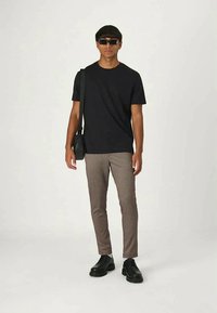 T-shirt preto de algodão com mangas curtas, calças xadrez castanhas e sapatos pretos com atacadores, acessorizado com óculos de sol pretos e um saco pequeno.