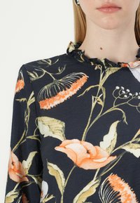 Blusa floral com um fundo escuro e flores em laranja e branco, detalhe de gola com babados e tecido macio e leve.