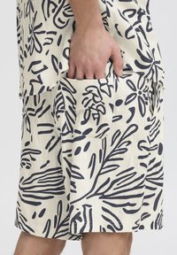 Light-colored shorts with a navy leaf pattern, made from fabric. Features a side pocket, relaxed fit, and a hem near the knee.