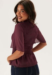 Fadets blouse i maroon med korte gennemsigtige ærmer, smock-detalje på ryggen og peplum-kant, lavet af letvægtsstof.