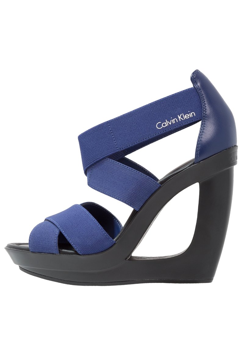 Sandales à talons compensés bleu marine avec des sangles élastiques, design à bout ouvert, et une plateforme noire contrastante. Elles présentent un talon courbé et un détail de logo.