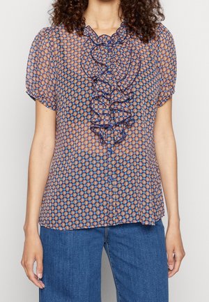 Niebieskawa bluzka w wzory z krótkimi rękawami, z falbaną z przodu i zapięciem na guziki. Materiał jest lekki i półprzezroczysty.