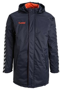 Manteau d'hiver bleu marine à capuche avec doublure orange, poches avant et bandes chevrons noires et blanches sur les manches, marqué "hummel" sur la poitrine.