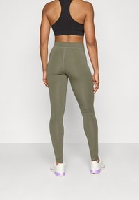 Leggings verde oliva con una cintura alta y una textura suave, combinados con un top corto negro y zapatillas blancas con acentos morados.