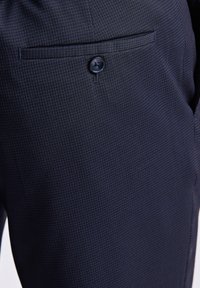 Pantaloni da completo a quadri blu navy con un fine motivo a griglia, dotati di tasca laterale, dettaglio con bottone e una texture raffinata.