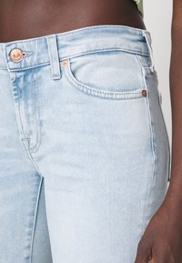 Helle blaue Jeans mit schmaler Passform, mittelhoher Taille, Kupferknopf-Beschlägen und subtilen Ausbleichungen der Stofftextur.
