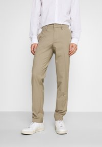 Beige Hosen aus leichtem Stoff mit geradem Bein und cleanen Fronttaschen, kombiniert mit weißen Sneakers.