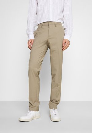 Pantaloni beige realizzati in tessuto leggero, con un design a gamba dritta e tasche frontali pulite, abbinati a sneakers bianche.
