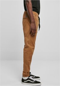 Kamelbrune bomuldsjoggers med elastisk talje, sidelommer og et lille mærke-logo på bagsiden. Sæt sammen med sorte sneakers.