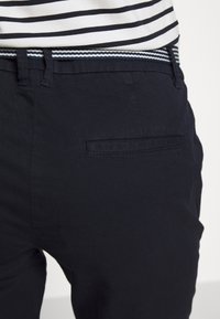 Námořnické modré bavlněné kalhoty s hladkou strukturou, se zadn í kapsou a pruhovaným látkovým pásem v námořnické, bílé a světle modré barvě.