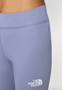Svijetloljubicaste tajice s glatkom teksturom, s širokim pojasom i bijelim logotipom The North Face na donjoj desnoj strani.