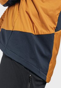Veste en color-block avec une partie supérieure orange brillante et une partie inférieure marine mate, réalisée en un matériau léger et résistant à l'eau.
