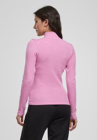 Enganliegendes, rosa Langarmoberteil mit hohem Kragen. Hergestellt aus geripptem Stoff, verfügt über ein nahtloses Design an den Schultern und eine glatte Textur.
