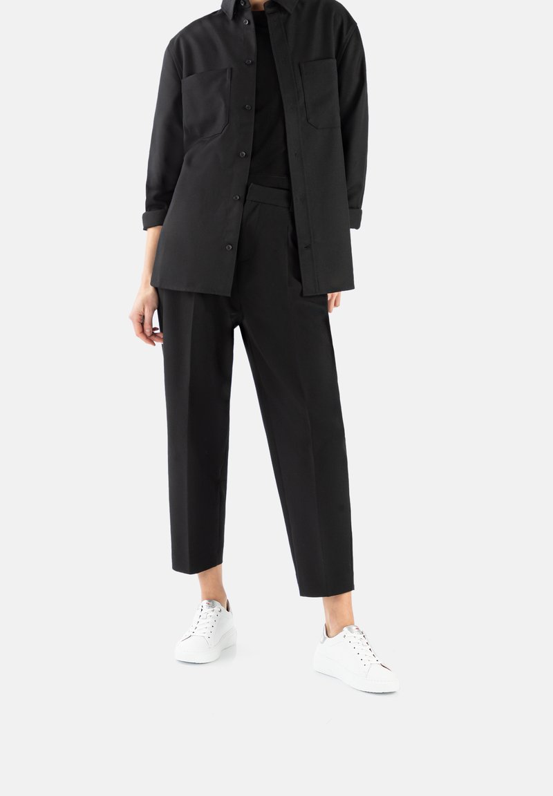 Black shirt and trousers made of smooth fabric, featuring a button-up design, two chest pockets, and white sneakers for contrast.