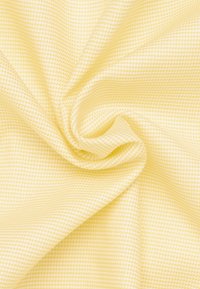 Tessuto giallo chiaro con una texture e un sottile motivo a quadri, che mostra una superficie liscia e morbida e cade in morbidi panneggi.