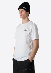 Hvid bomulds T-shirt med korte ærmer, prydet med et lille sort logo på brystet, kombineret med en sort ribbet hue.
