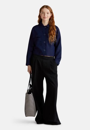 Veste cropped marine avec fermeture à boutons ; large pantalon noir ; sac à main rayé avec des couleurs contrastantes. Texture de tissu lisse, coupe décontractée.
