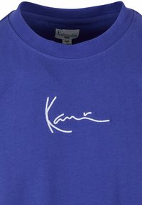 Violet medvilninis marškinėliai su apvalia kaklo iškirpte ir balta siuvinėta parašu logo priekyje. Lygus paviršius ir kasdieniškas dizainas.