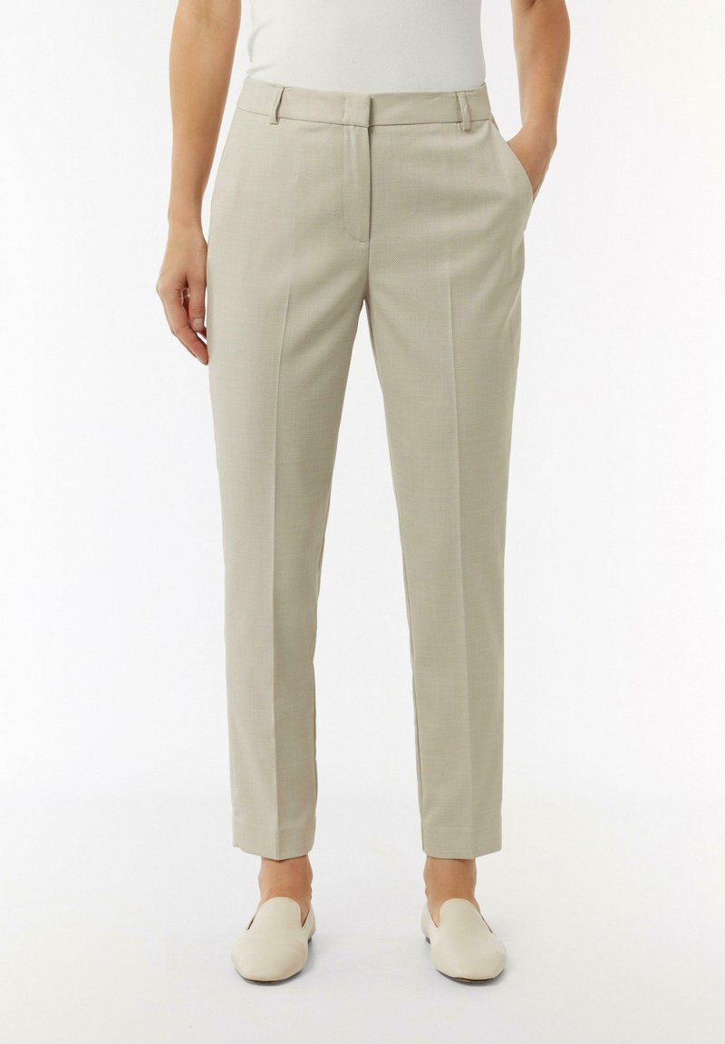 Beżowe, dopasowane spodnie z subtelną teksturą, slim fit, z kieszeniami po bokach i przeszywaną kantem. Noszone z jasnymi, wsuwanymi butami.