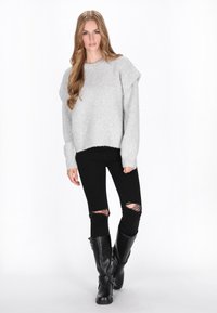 Lys grå oversized striktrøje med ribkant, parret med sorte ripped skinny jeans og knæhøje sorte læderstøvler.