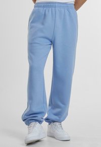 Helles blaues Baumwoll-Sweatpants mit einem elastischen Bund und Knöchellöchern, mit Seitennähten und kombiniert mit weißen Turnschuhen.