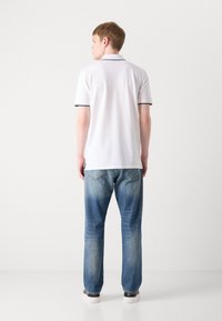 Polo bianco con bordi neri su colletto e maniche, abbinato a jeans in denim blu. Modello rivolto di spalle, che mostra la vista posteriore.